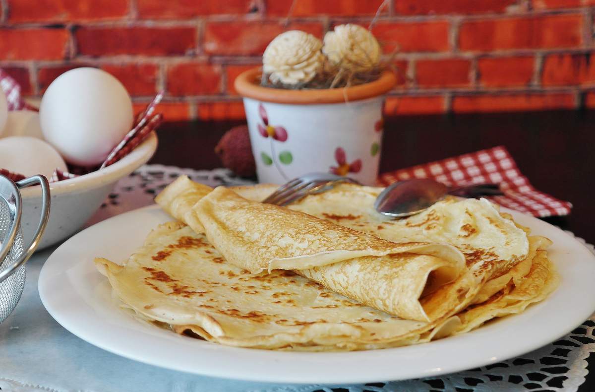 Crepes sobre um prato branco em uma mesa posta.